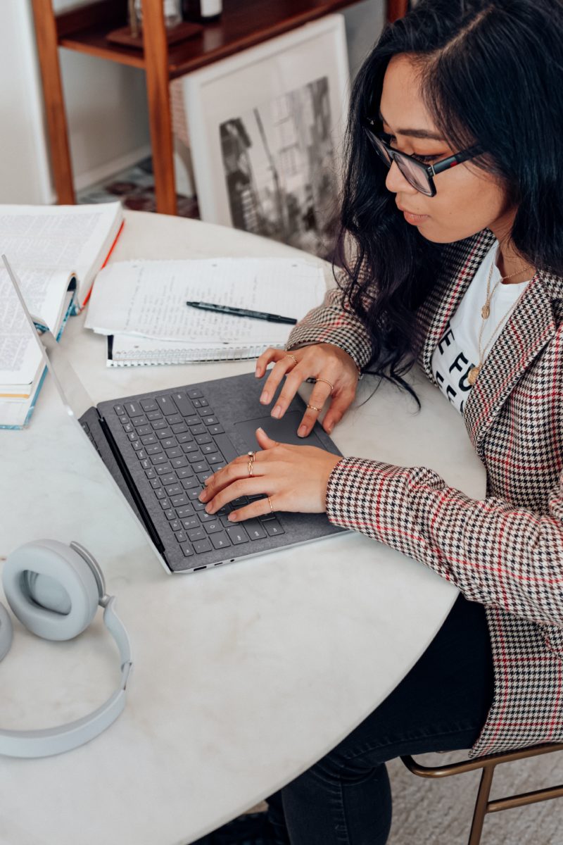 woman in red and white plaid long sleeve shirt using platinum coloured microsoft surface laptop computer